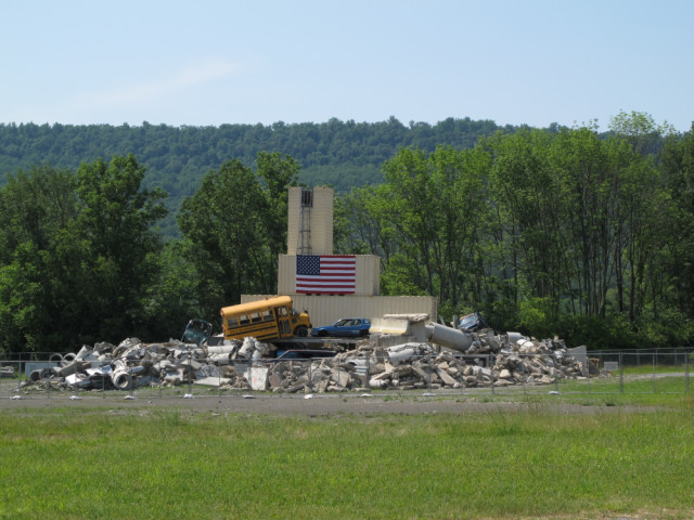 A conglomeration of a bus, a car, some box trailers, and concrete chunks.